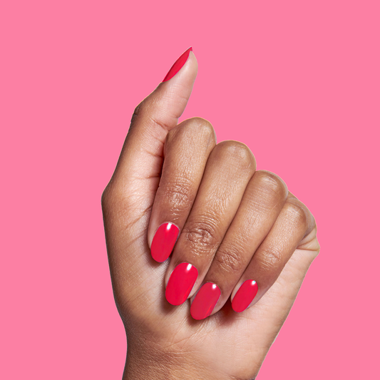 Hand with nails painted in glossy Hibiscus polish by Olive and June showing bright tropical pink manicure on solid pink background