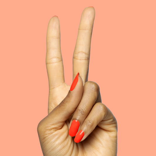 Two fingers showing a peace sign with nails painted in bright orange-red Snapdragon quick dry polish on peach background