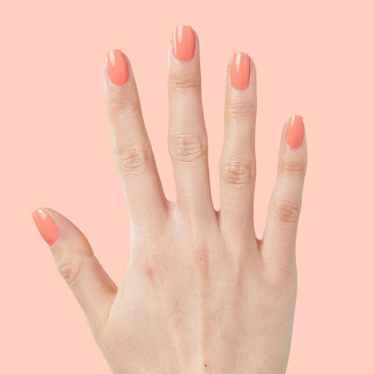 Hand with nails painted in bright cantaloupe orange Counselor In Training gel polish on pale peach background