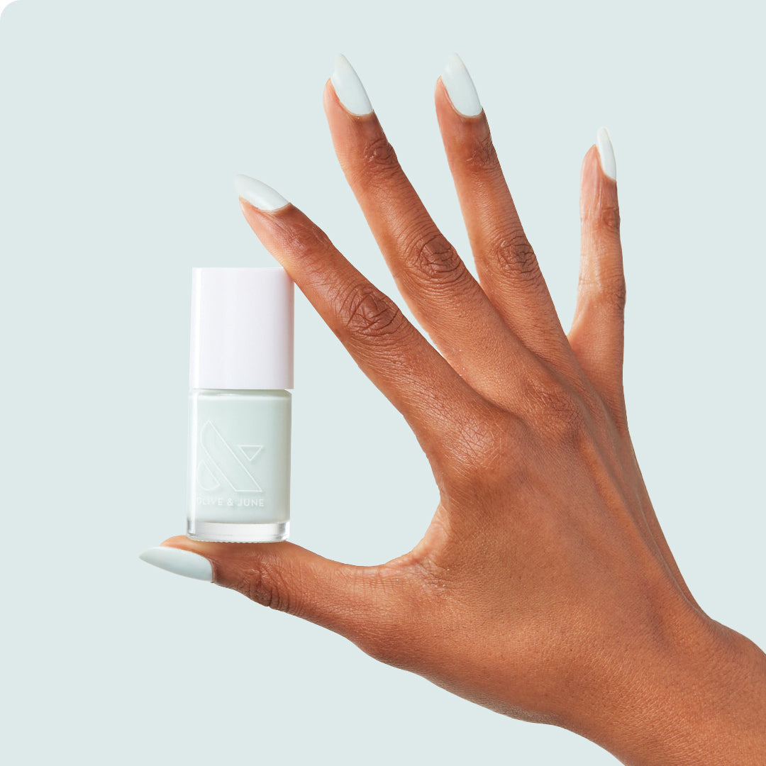 Hand with nails painted in pastel mint green Sleeping Bag long-lasting gel polish holding polish bottle on pale blue background