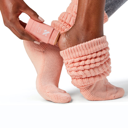 Person applying Overnight Heel Repair Set balm to heel while wearing textured peach knit socks on white background