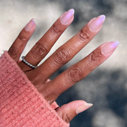 Hand with long almond-shaped nails painted in Baroque gel polish showing subtle pearly iridescent manicure outdoors