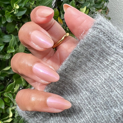 Hand with almond-shaped nails polished in milky golden iridescent Sandy Scallop gel polish wearing a gold ring and gray sweater
