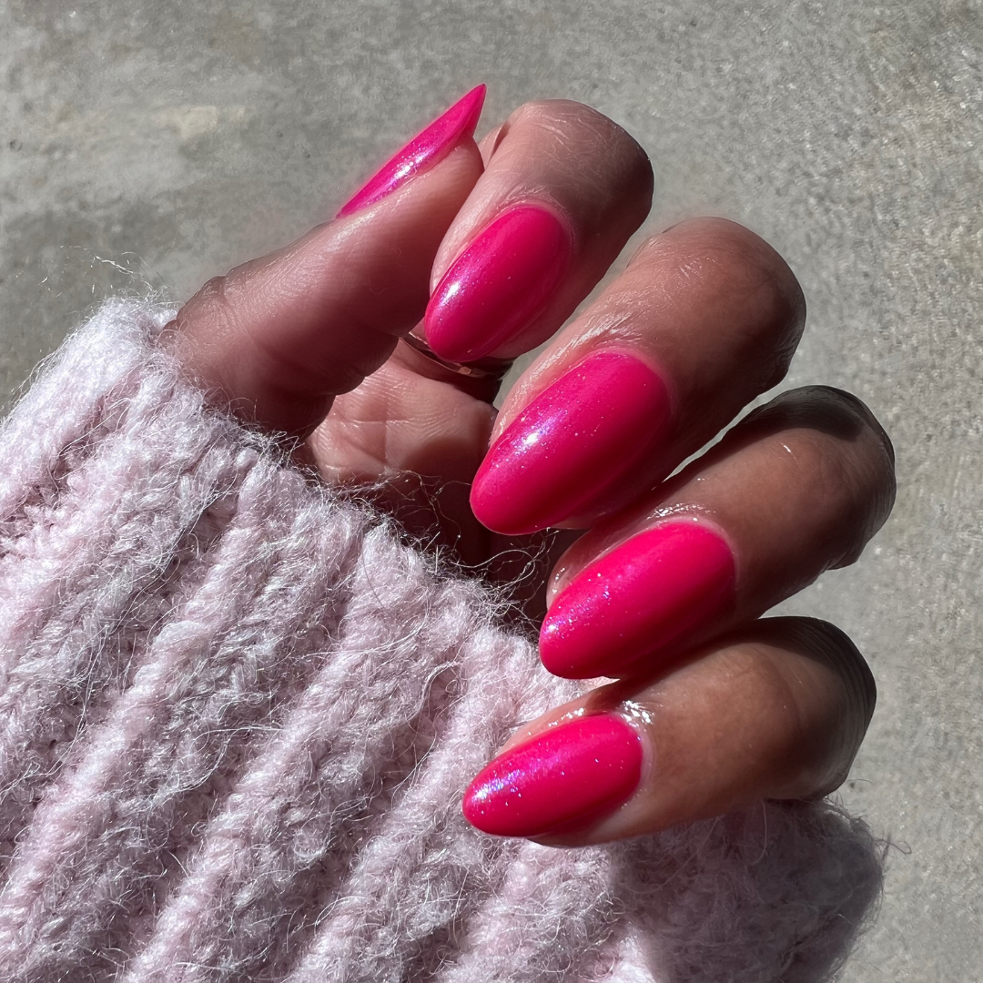 Hand with almond-shaped nails painted in glossy Berries sheer berry-pink gel polish showing smooth at-home mani outdoors