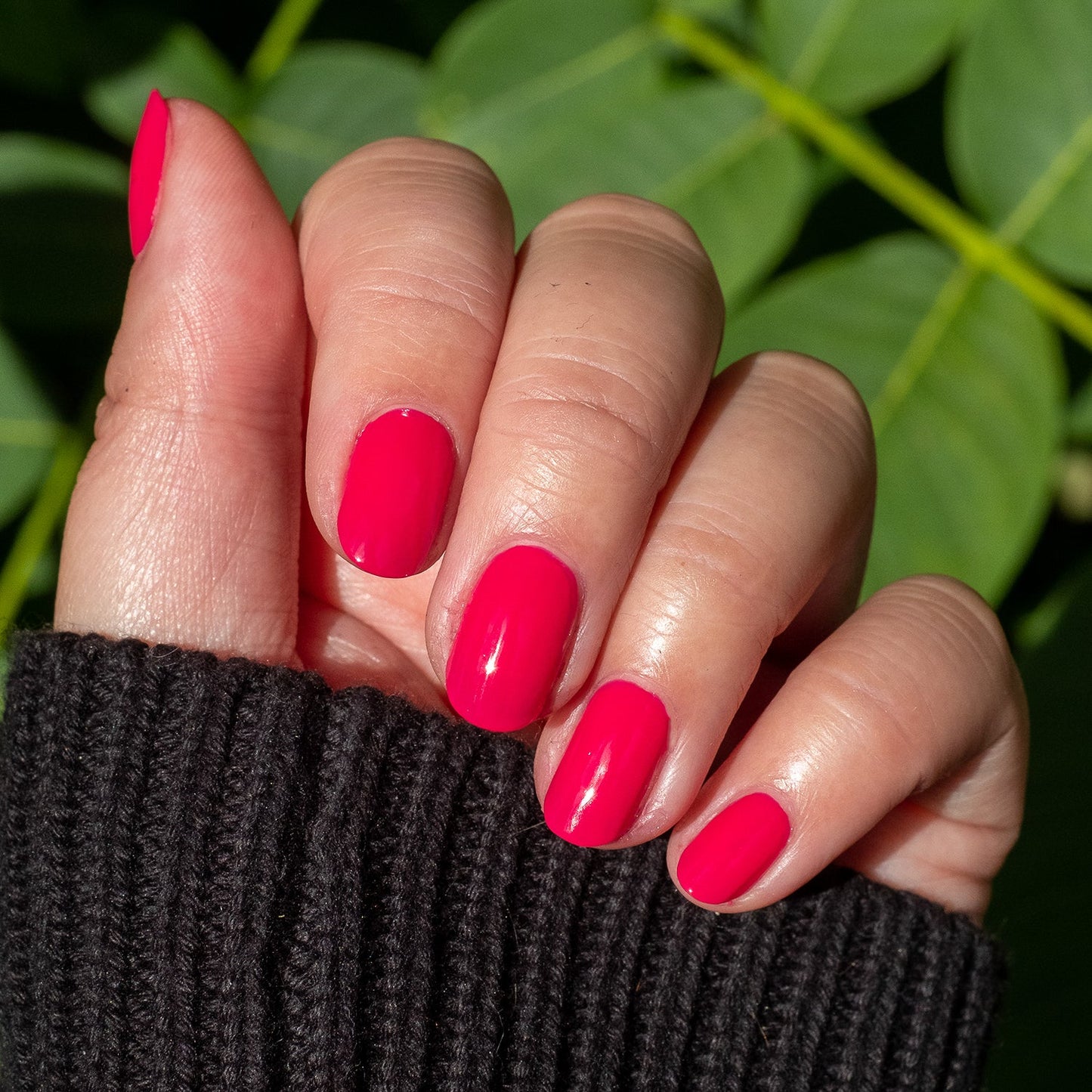 Hand displaying smooth nails painted with XOXO hot pink polish for a bright, long-lasting manicure outdoors