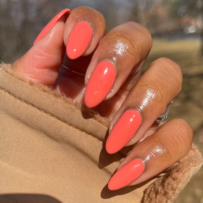 Hand with long almond-shaped nails painted glossy Carrot Juice gel polish by Olive and June outdoors in natural light