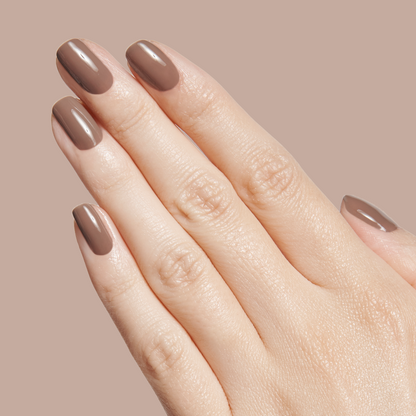 Hand with nails painted in Fawn - Gel, a glossy minky brown neutral gel polish against a matching beige background