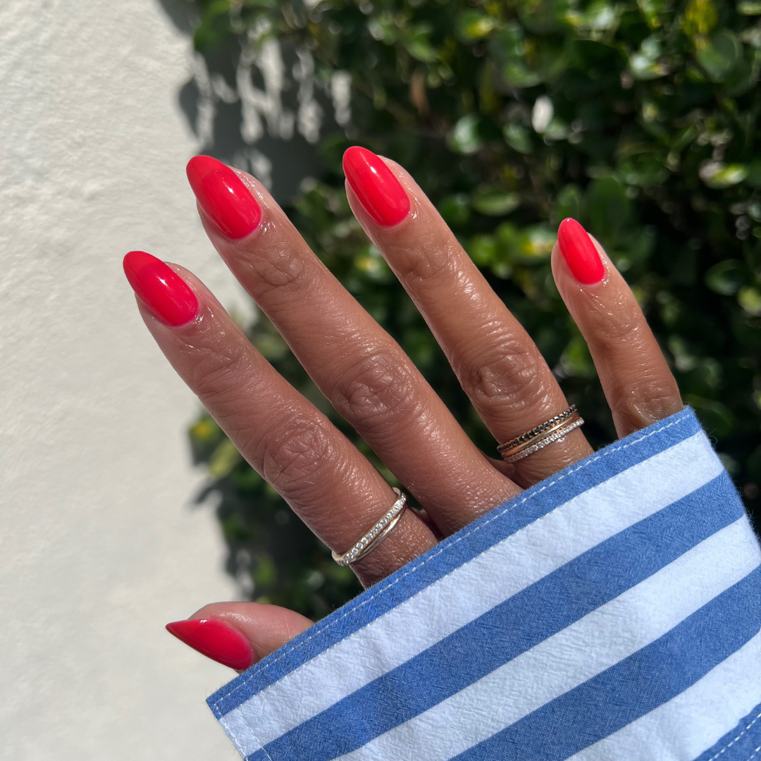 Hand with almond-shaped nails painted in glossy Fragola polish showing smooth at-home mani in sunlight outdoors