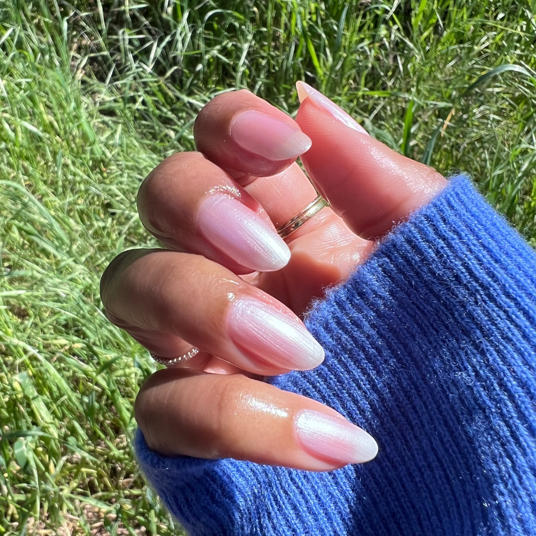 Hand with almond-shaped nails polished in sheer pearly Freshwater gel polish showing a natural mani outdoors