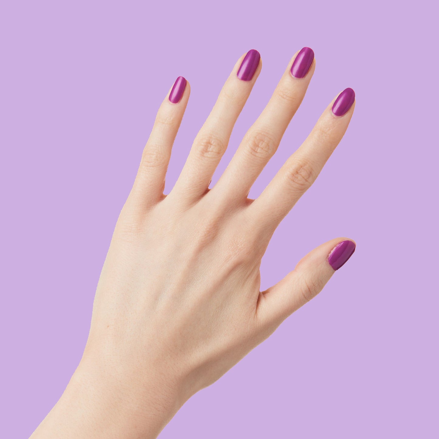 Hand with nails painted vibrant purple Grape Soda polish showing smooth, glossy manicure against lavender background