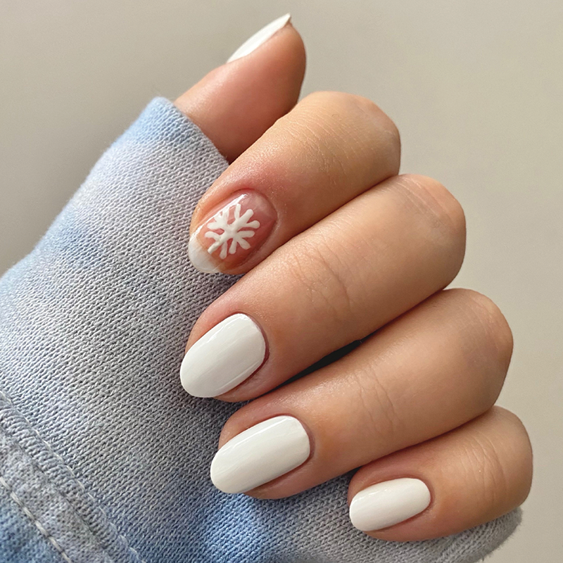 Hand with short nails painted in HD polish crisp white with one accent nail featuring a subtle snowflake design