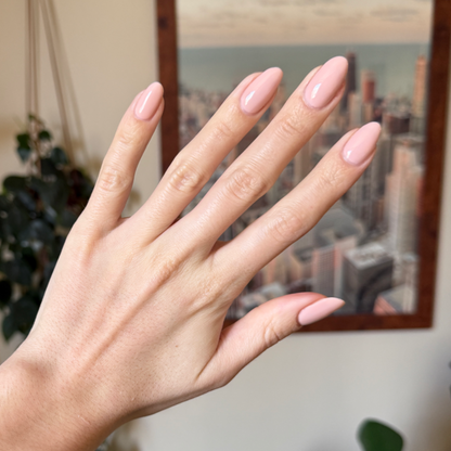 Hand with almond-shaped nails painted in KAG - Gel neutral peachy pink gel polish against blurred cityscape background