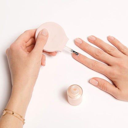 Hand using The Poppy universal polish bottle handle to apply nude nail polish for easier at-home mani control