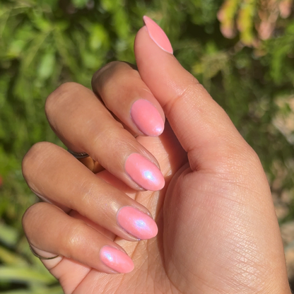 Hand with short almond-shaped nails painted in sheer pink-blue iridescent Olive Y'all gel polish manicure outdoors