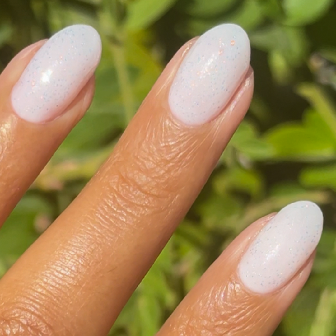 The Pixie Effect Top Coat adding a delicate iridescent shimmer over soft white polish for a unique manicure finish