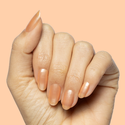 Hand with natural nails coated in Sunlit warm golden peach shimmer gel polish on a soft peach backdrop