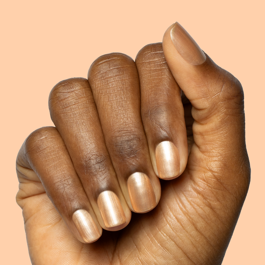 Hand with short rounded nails painted in Sunlit warm golden peach shimmer gel polish on peach background