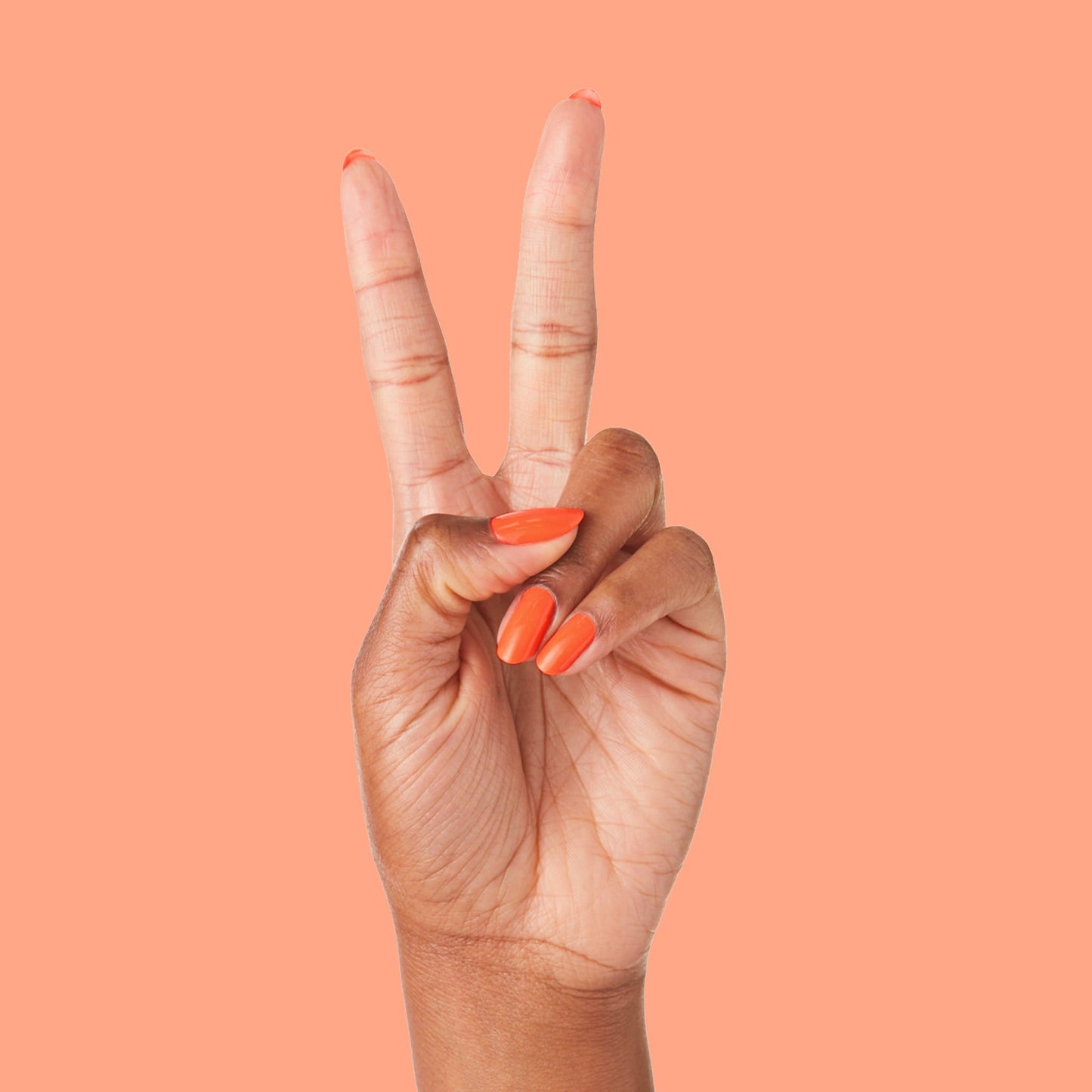 Hand with nails painted in bold tangerine You're a 10 gel polish showing fresh manicure on peach background