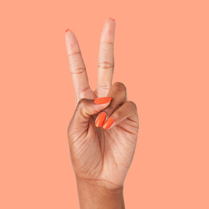 Hand with nails painted in bold tangerine You're a 10 gel polish showing fresh manicure on peach background