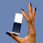 Hand with glossy navy blue gel polish holding a bottle of Ack, A Shark! long-lasting nail polish by Olive and June