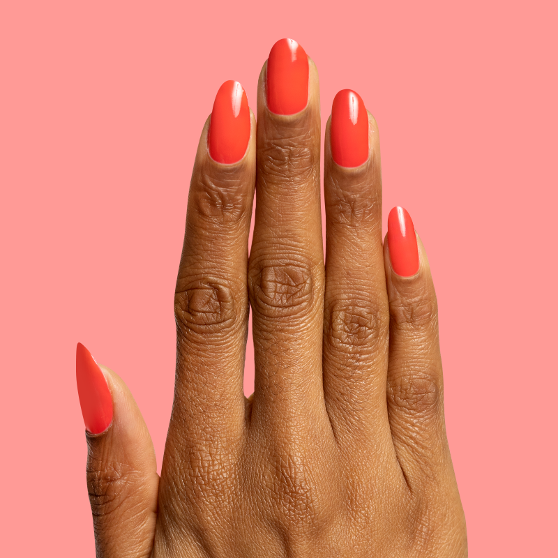 Hand with glossy Fragola nail gel polish in bold strawberry pink showing smooth manicure against coral background