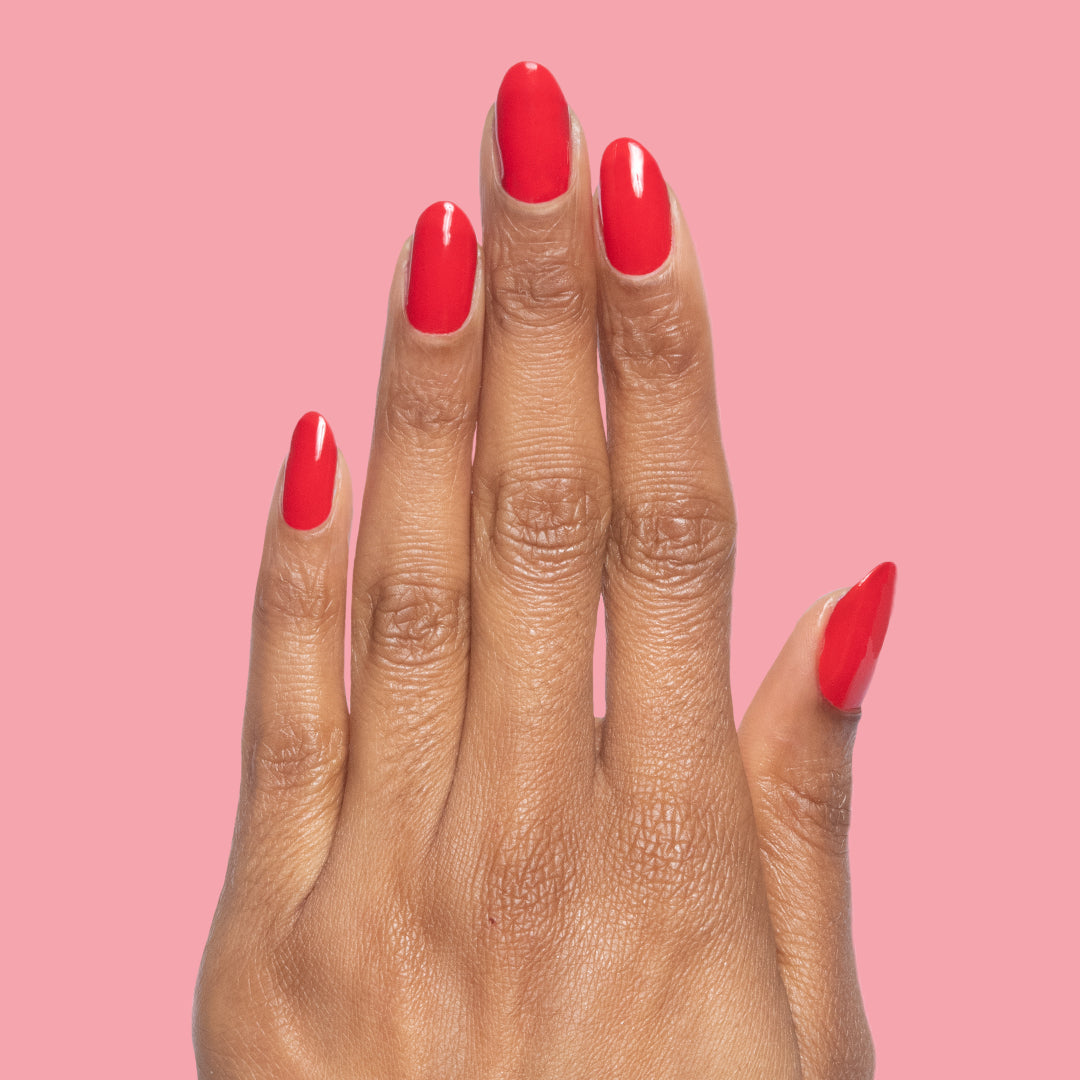 Hand with nails painted in glossy cherry red Lollipop quick dry polish against a soft pink background