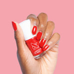 Hand with glossy cherry red nails holding Lollipop quick dry polish bottle on soft pink background
