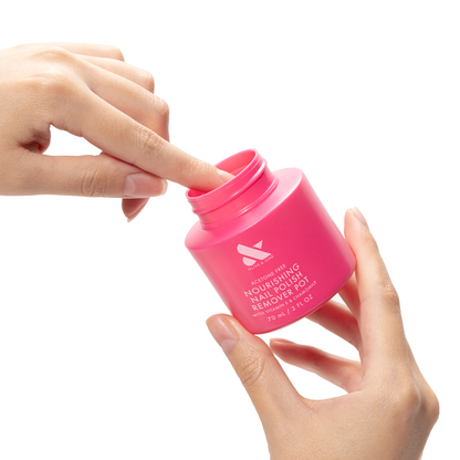 Hands dipping a finger into a bright pink Nourishing Remover Pot for quick, nourishing nail polish removal with care ingredients