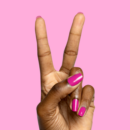 Hand with nails painted in vibrant orchid magenta Wildest gel polish showing glossy, bold mani on pink background